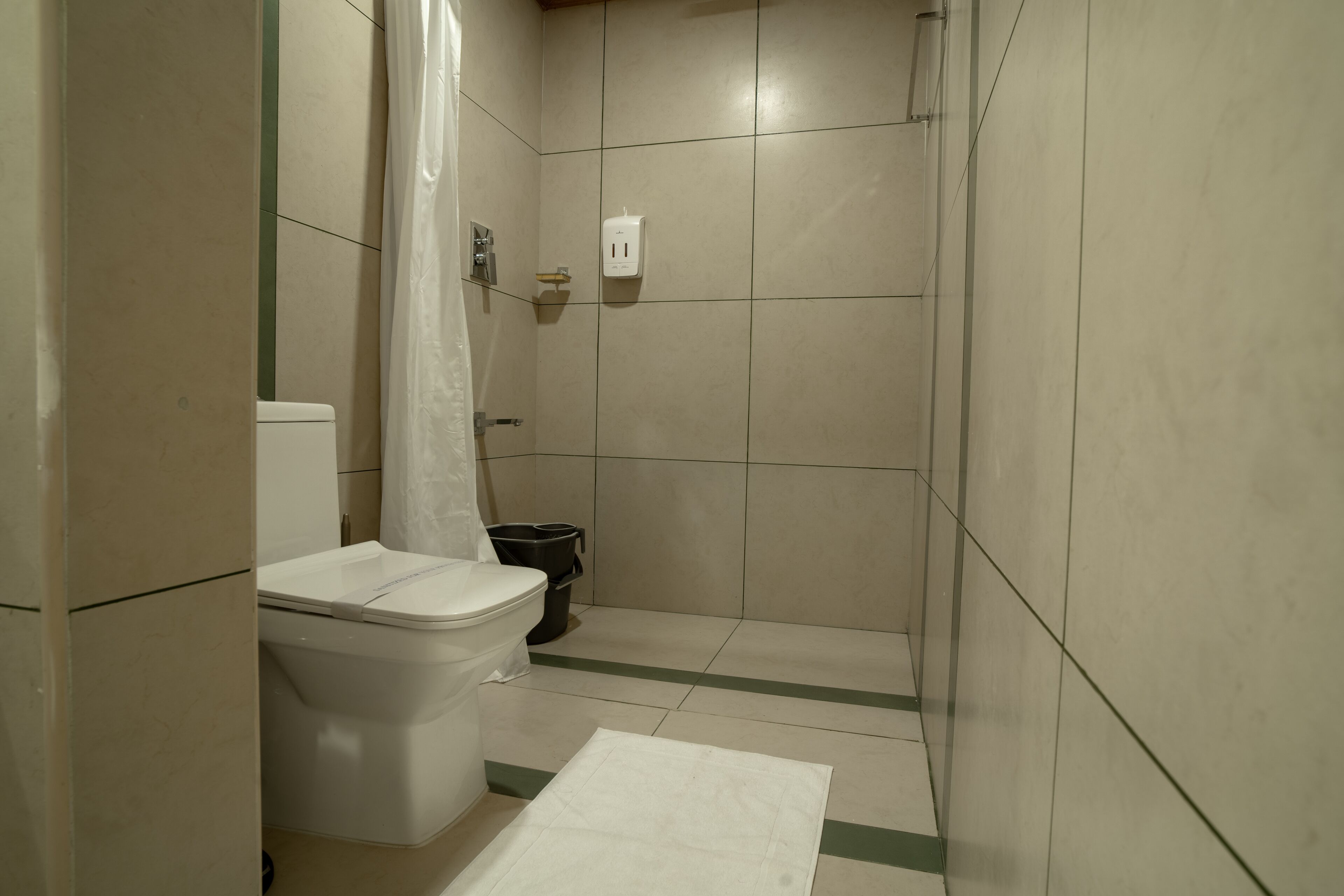 A bathroom with a toilet, a shower area, and a waste bin.