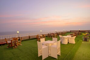 An outdoor seating area with tables and chairs, a railing, and a view of the sea.
