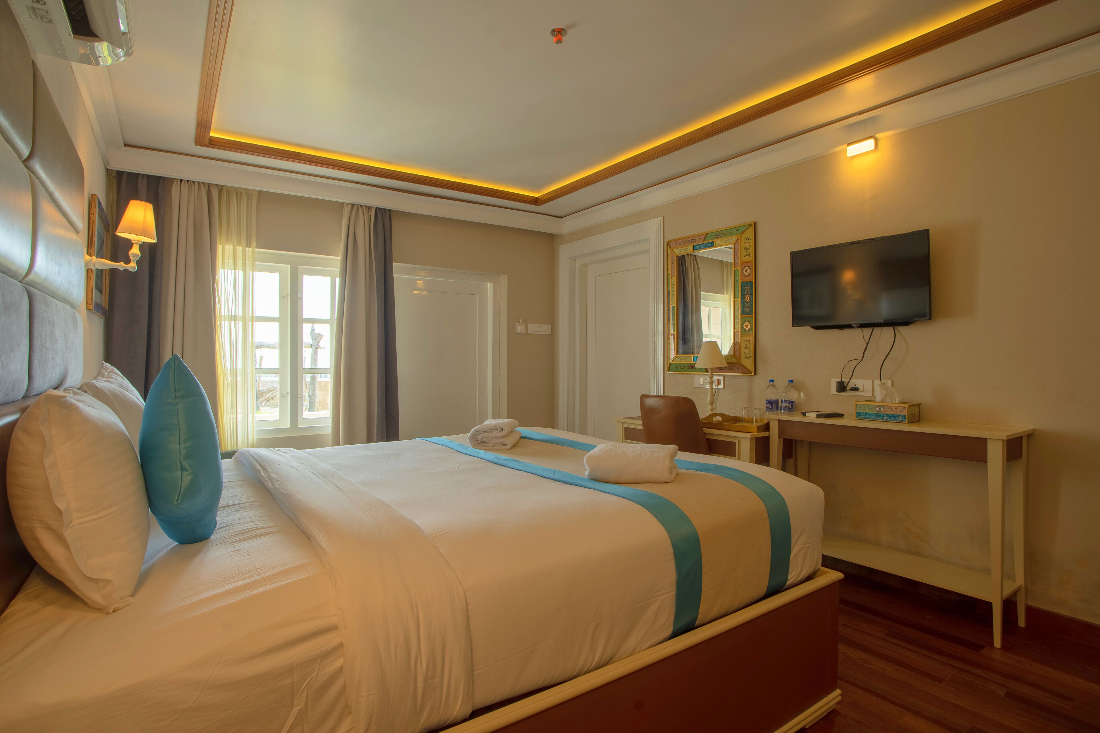 A hotel room with a large bed, a desk with a chair, a television, and a window with curtains.