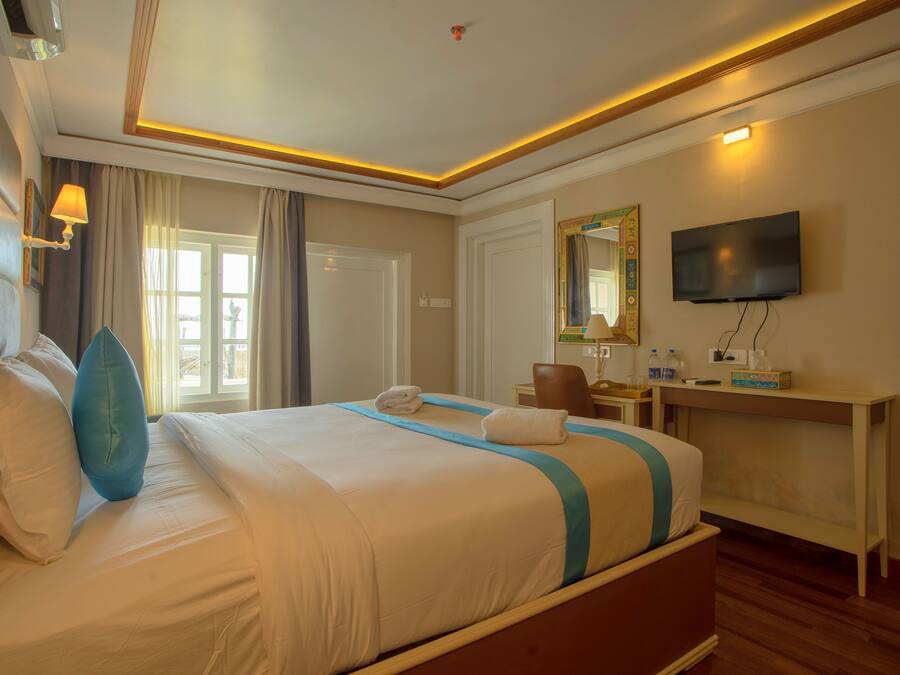A hotel room with a large bed, a desk with a chair, a television, and a window with curtains.
