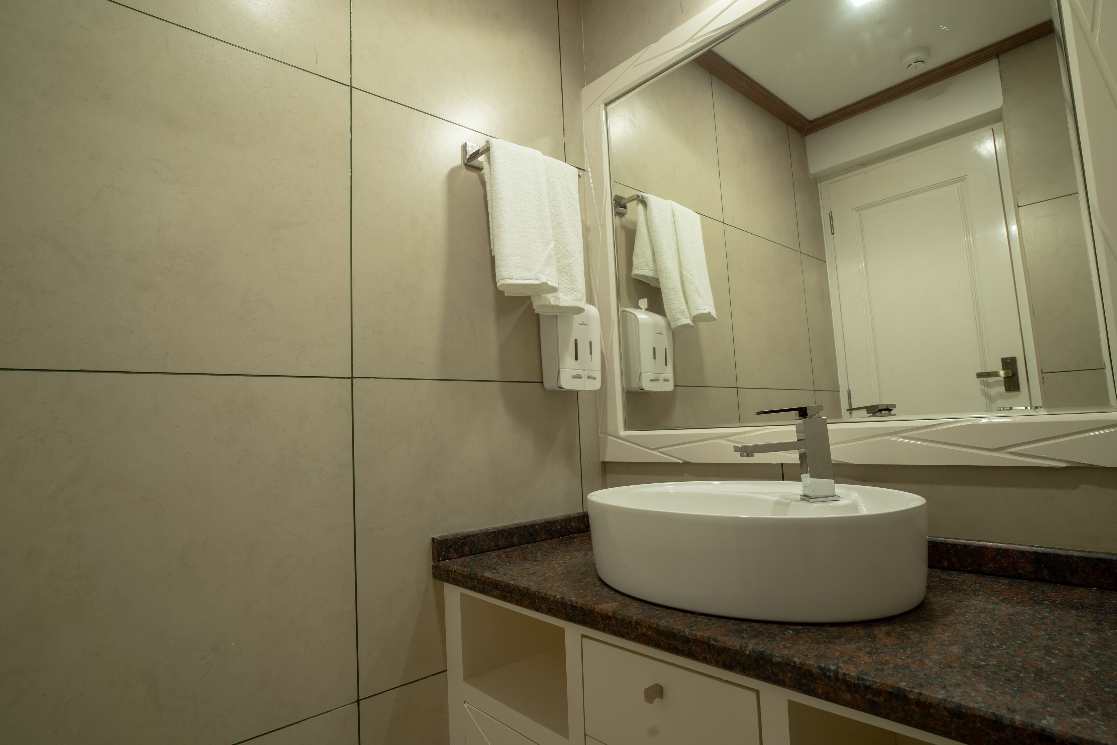 A bathroom with a round white sink, a mirror above it, and a towel rack with two towels.