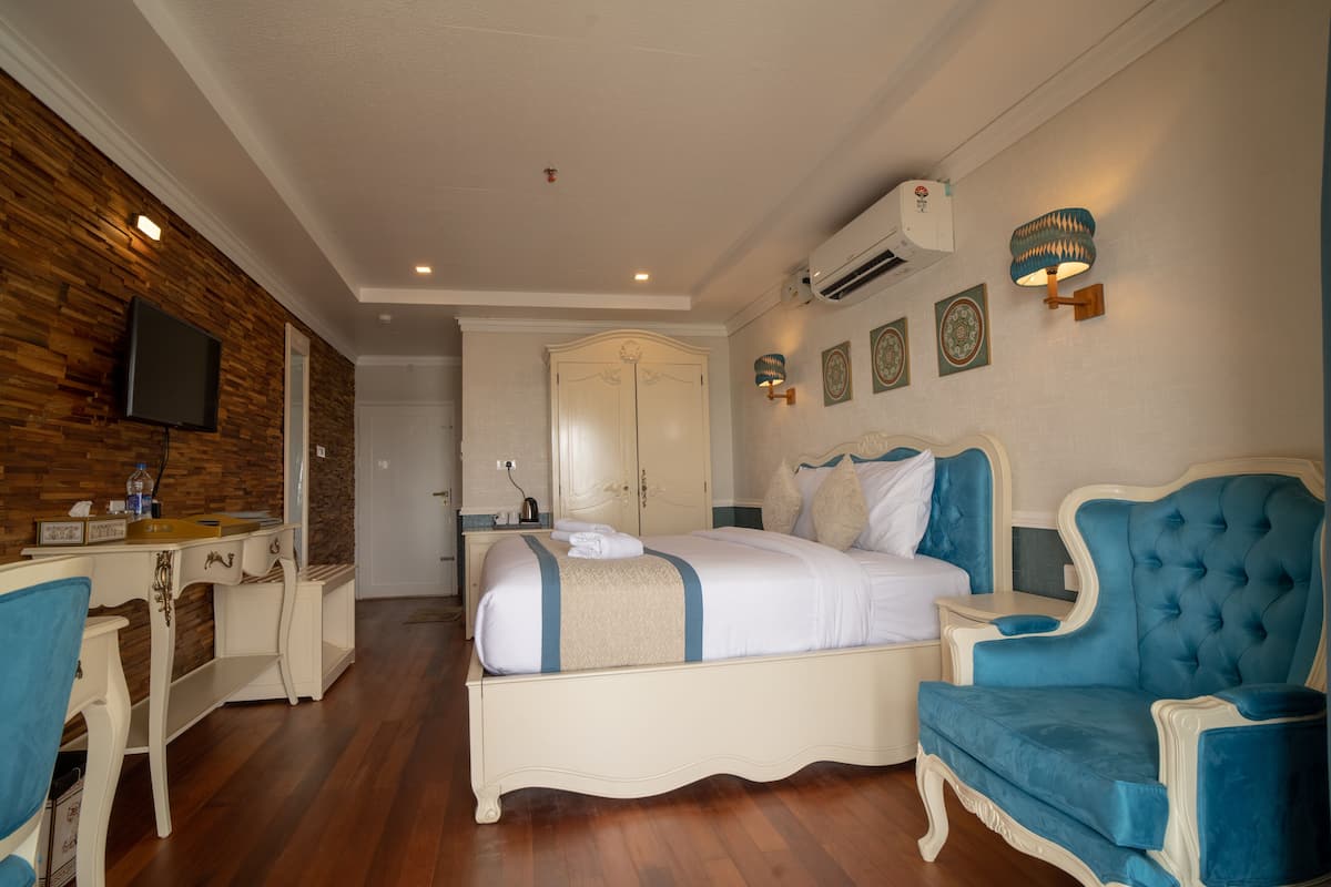 Una habitación de hotel con cama, escritorio, silla, armario e iluminación en la pared.