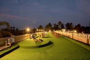 A rooftop terrace with artificial grass, lounge chairs, and tables.