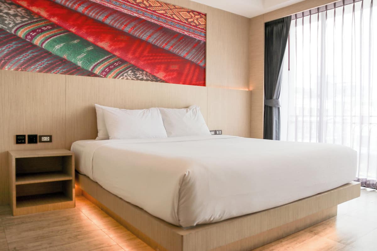 A modern hotel room with a large bed, a nightstand, and a wall-mounted tapestry.