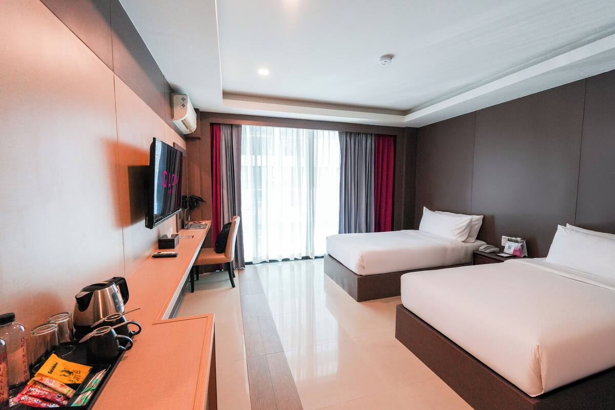 A hotel room with a bed, bedside table, TV, and a window with curtains.