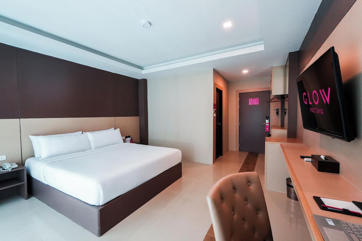 A modern hotel room with a large bed, a desk with a chair, a television, and a bathroom visible in the background.
