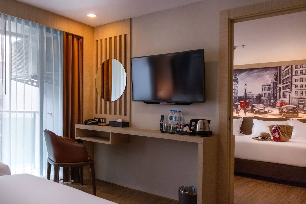 A hotel room with a bed, a desk with a TV, a chair, a mirror, and a painting of a cityscape.