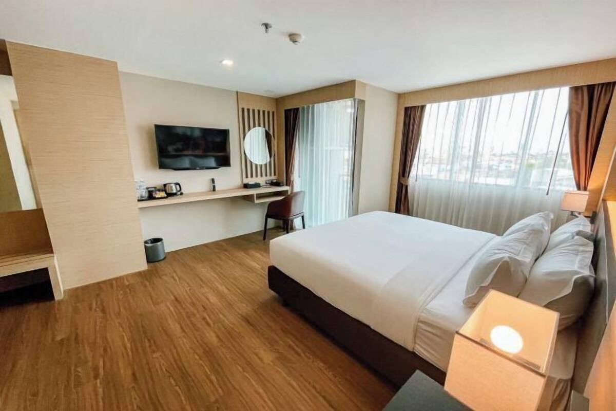 A hotel room with a large bed, a desk with a chair, a television, and a window with curtains.