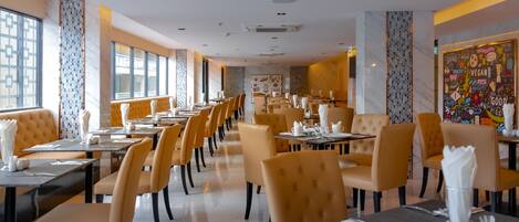 Restaurante com várias mesas e cadeiras, parede revestida de azulejos e um mural.