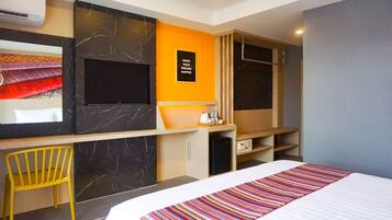 A hotel room with a bed, a desk, a chair, a TV, and a motivational poster on the wall.