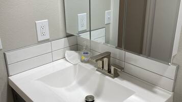 A bathroom with a white sink, a mirror, and a soap dispenser.