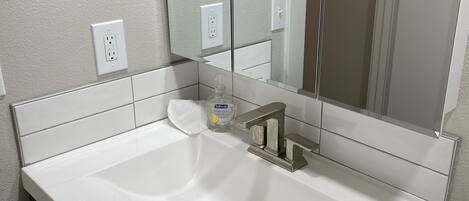 Une salle de bain avec un lavabo blanc, un miroir et un distributeur de savon.