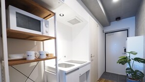A compact kitchen with a microwave, sink, and wooden shelves. - Luana Shibuya (Tokyo)