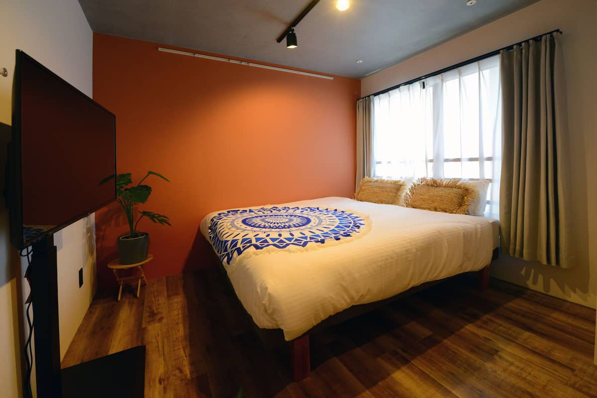 Quarto com cama, um vaso de planta e uma TV sobre um suporte.