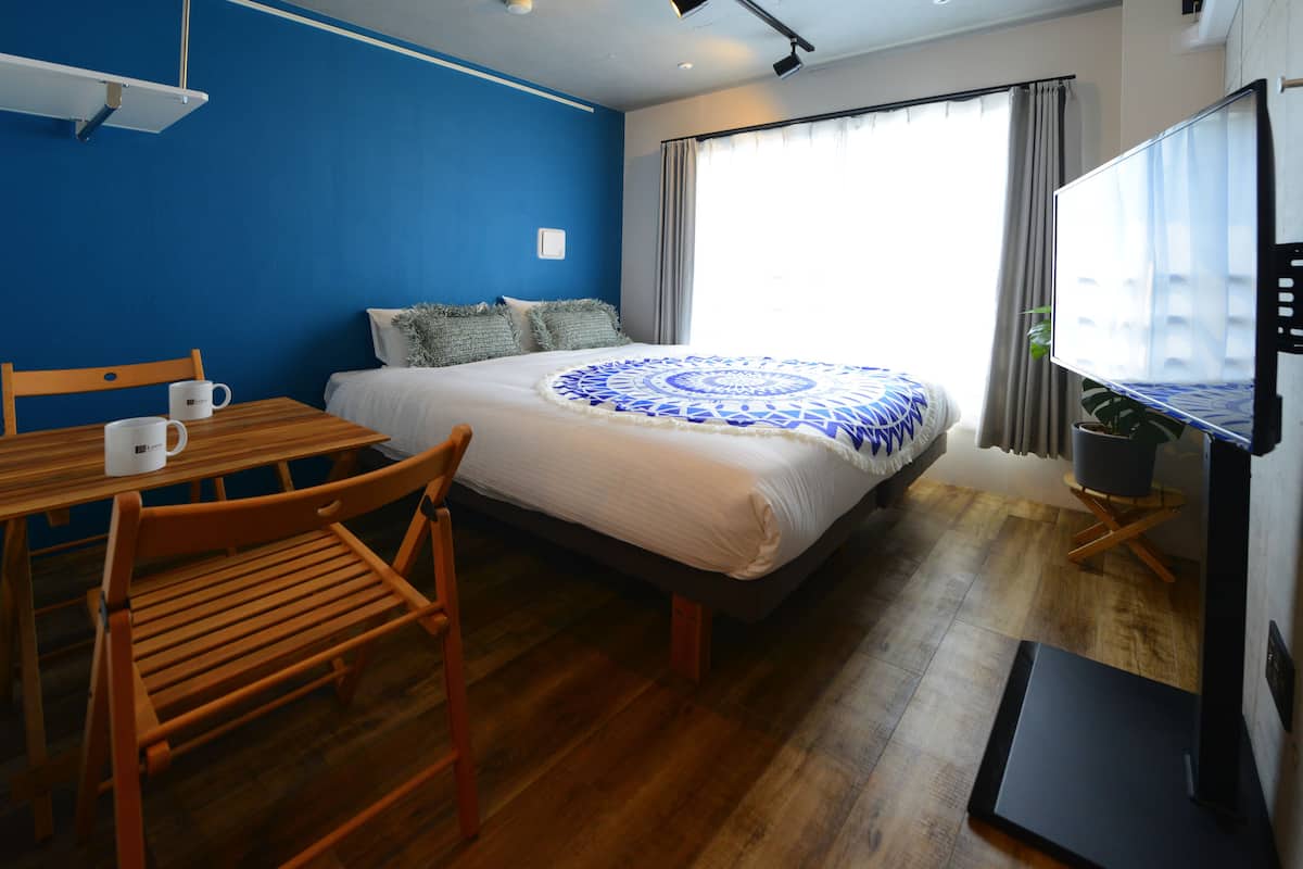 Quarto de hotel com cama, mesa de madeira com cadeiras, televisão e janela com cortinas.