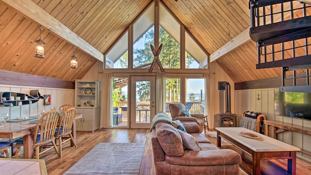 A spacious loft-style living area with a high ceiling, wooden beams, a large sofa, a dining table, and a fireplace.