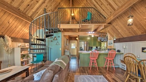 A spacious loft with a wooden interior, a spiral staircase, a cozy living area with a sofa, and a kitchen with bar stools.