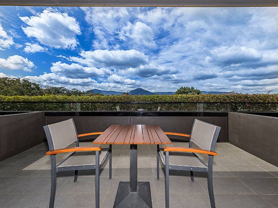 A patio with a table and two chairs, a view of a mountain, and a cloudy sky.