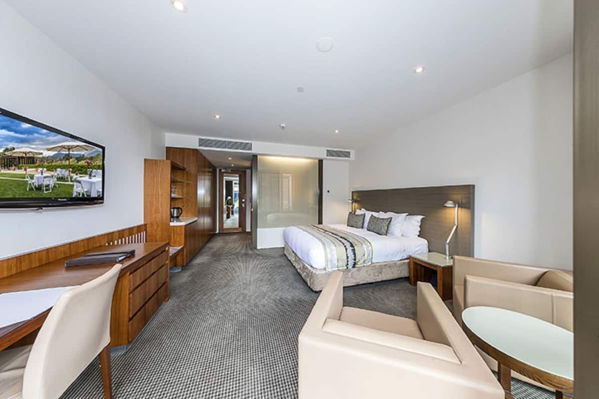 A hotel room with a bed, a desk, a chair, a TV, and a view of the outdoors.