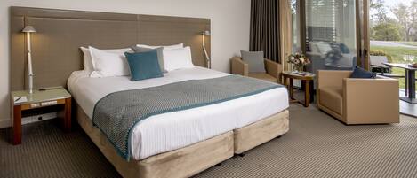 A hotel room with a large bed, a desk, a chair, and a view of the outdoors.