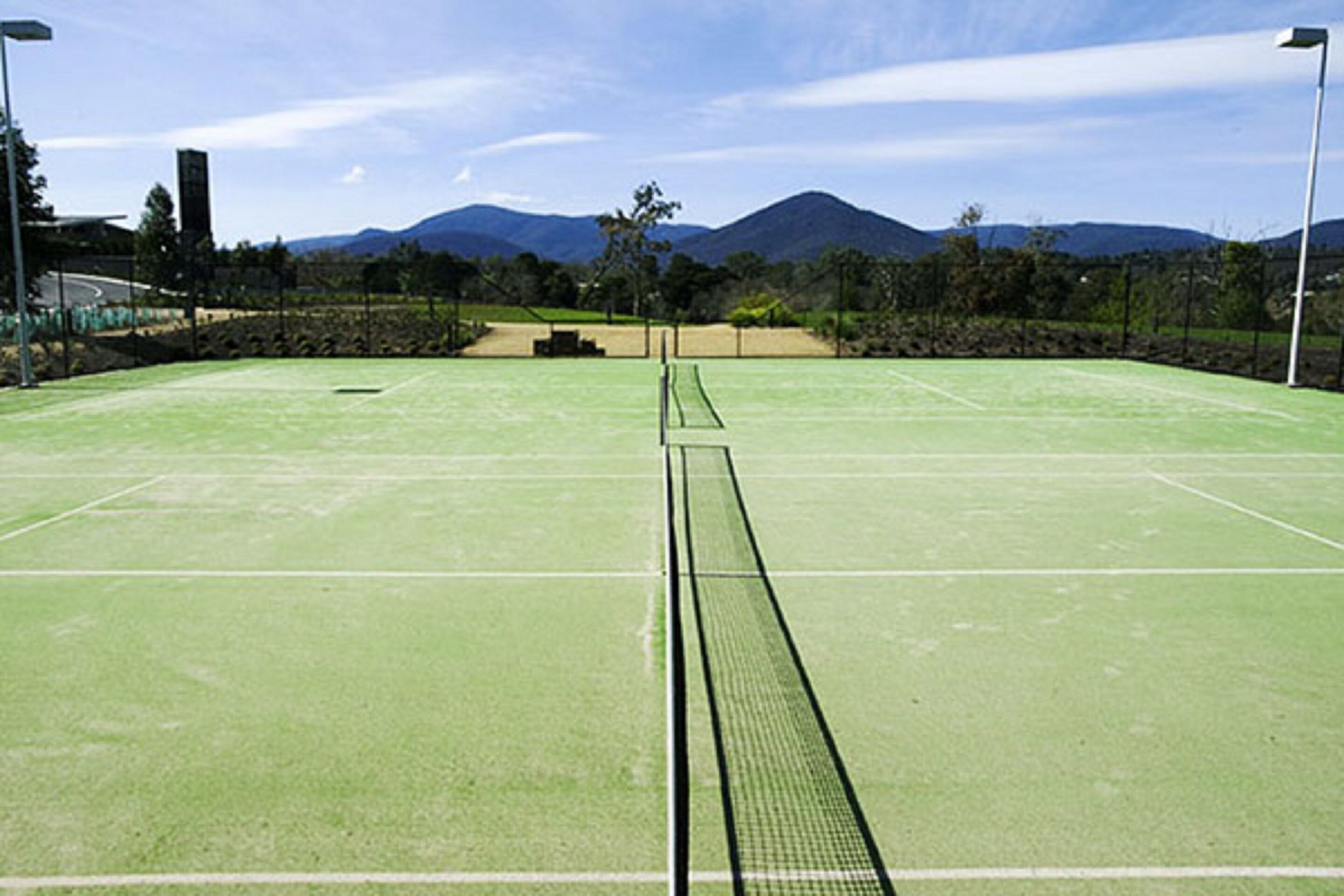 A tennis court with a net, surrounded by trees and mountains in the background.