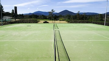 A tennis court with a net, surrounded by trees and mountains in the background.