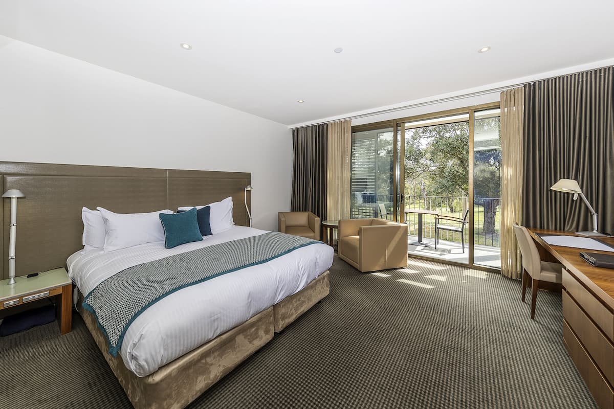 A hotel room with a large bed, a desk, a chair, and a balcony with a view of the outdoors.