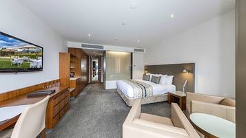 Habitación de hotel moderna con cama, escritorio, silla, televisor y vistas al exterior.