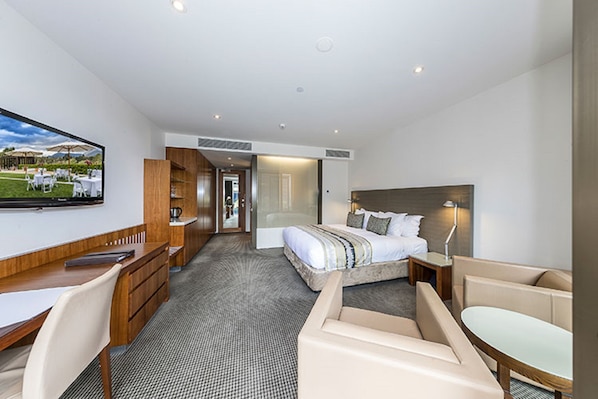 A modern hotel room with a bed, a desk, a chair, a TV, and a view of the outdoors. - RACV Healesville Country Club & Resort (Healesville)