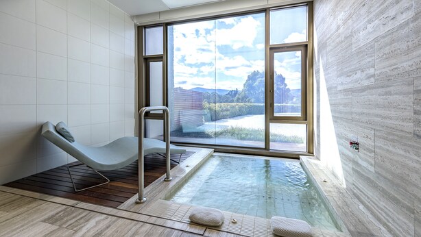 Une salle de spa moderne dotée d’un jacuzzi entouré de parois de verre, d’un fauteuil inclinable et offrant une vue sur l’extérieur.