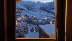 A window view of a snow-covered mountain town at dusk, with buildings and a ski lift visible. - Prestigious ski-in/ski-out apartment with panoramic view (Huez)