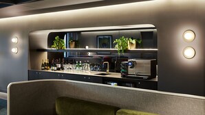 Zona de bar moderna con un diseño elegante, que incluye una barra, botellas de vino, copas y una máquina de café.