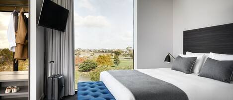 A modern hotel room with a large bed, a flat-screen TV, a view of the outdoors, and a seating area with a suitcase.