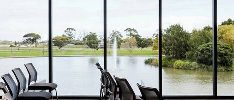 A conference room with a view of a lake and fountain, featuring modern chairs and a large window.