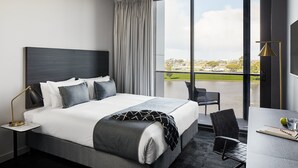 Habitación de hotel moderna con una cama grande, un escritorio con silla y vista a la ciudad a través de un ventanal.