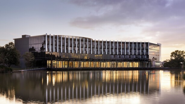 Un hotel moderno con una piscina reflectante al frente, que presenta una fachada curva y grandes ventanales.