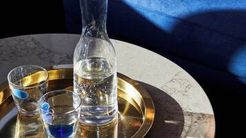 A round table with a marble top, a gold tray, a clear glass pitcher, and two shot glasses filled with a blue liquid.