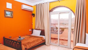 A hotel room with a bed, a small table, a chair, an air conditioning unit, a picture frame, and a sliding glass door leading to an outdoor area. - Dahab Plaza Hotel (Dahab)