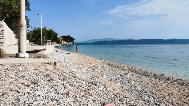 A pebble beach with a stone pillar, a clear sky, and distant mountains. - QueenSuite (Živogošće)