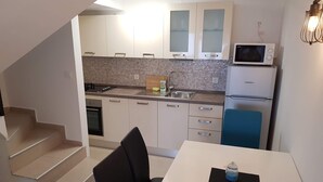 A compact kitchen with white cabinets, a microwave, a refrigerator, and a sink. There is a dining table with two chairs and a small rug. - QueenSuite (Živogošće)