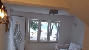 A compact living space with a sofa, a dining table, and a view of the sea through large windows. - QueenSuite (Živogošće)