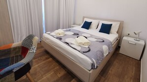 A hotel room with a bed, a chair, an air conditioning unit, and a nightstand with a lamp. - QueenSuite (Živogošće)