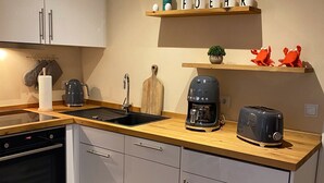 Cuina moderna amb armaris blancs, tauleig de fusta, cafetera, torradora i prestatgeria amb objectes decoratius.
