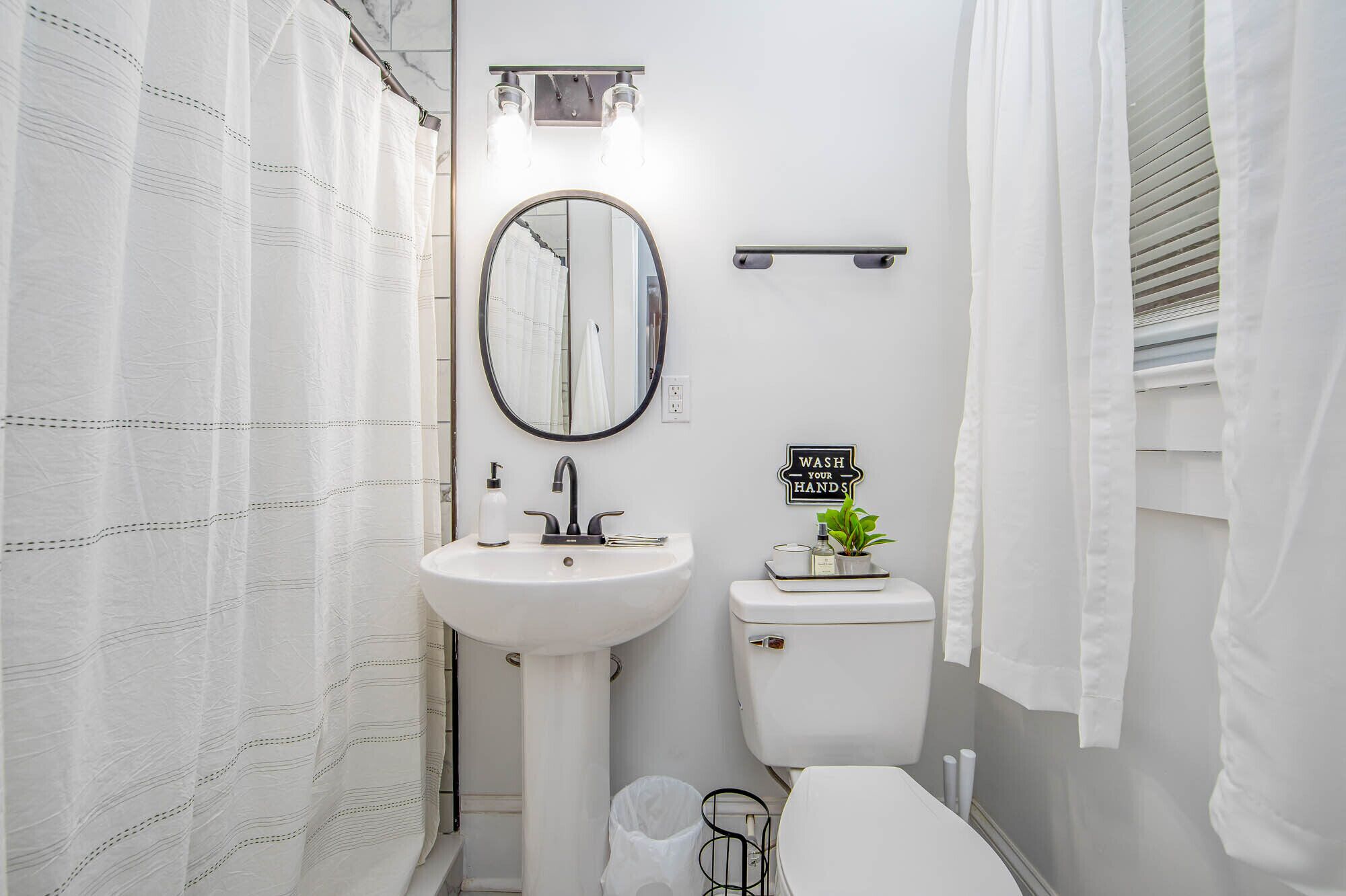 A compact bathroom with a white sink, a toilet, a mirror, and a 'WASH YOUR HANDS' sign.