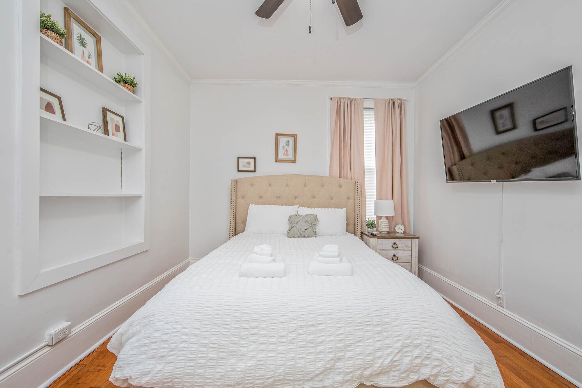 Une chambre bien rangée, avec un lit, des tables de chevet, une télévision et un ventilateur de plafond.
