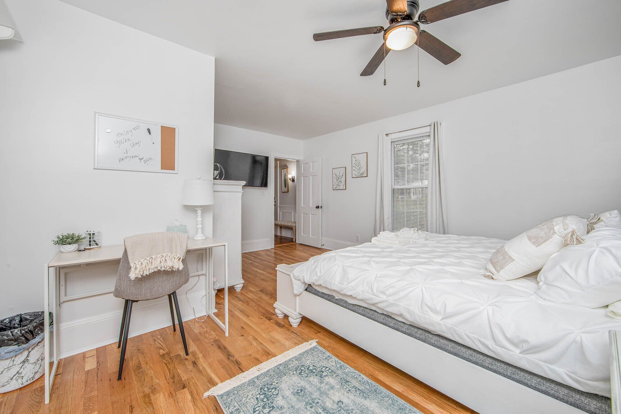 A bedroom with a bed, a desk, a chair, a ceiling fan, and a window with blinds.