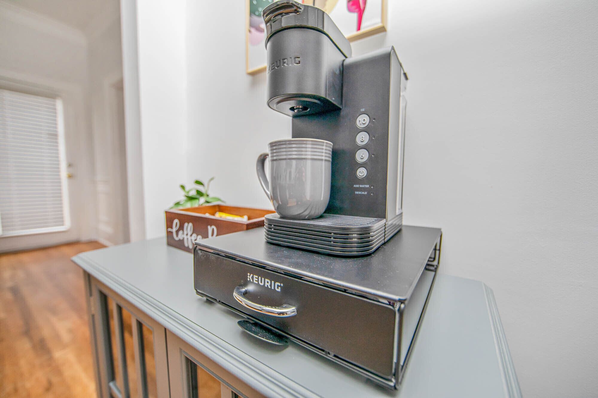 A Keurig coffee maker on a cabinet with a coffee mug and a box labeled "Coffee."