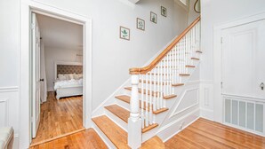 Eine Treppe mit weißen Balustraden und Holzstufen führt zu einem Schlafzimmer mit einem Bett und einem Nachttisch.