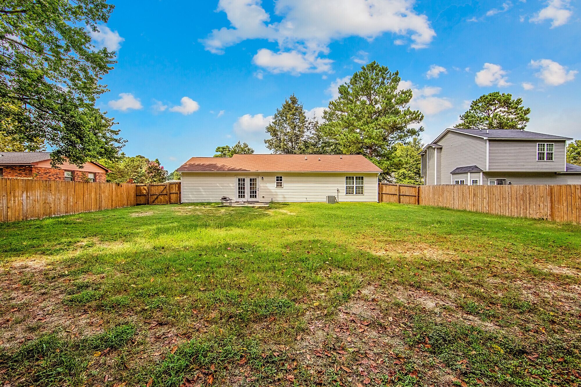 A residential backyard with a lawn, a wooden fence, and two houses.