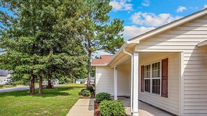 A single-story house with a covered porch, a well-maintained lawn, and mature trees. - The Strickland Stopover (Fayetteville)
